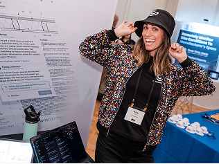 A photo of Molly at a tradeshow wearing a fun, sparkly jacket and Constructablebucket hat